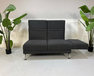 Erneuertes graues Brühl Moule Designer Stoff Sofa vor einer Wand, stilvoll und modern eingerichtet.