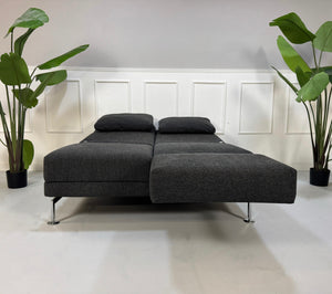 Erneuertes graues Brühl Moule Designer Stoff Sofa vor einer Wand, stilvoll und modern eingerichtet.