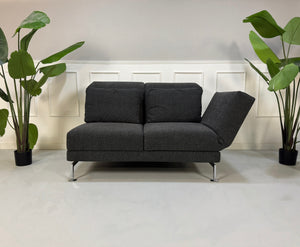Erneuertes graues Brühl Moule Designer Stoff Sofa vor einer Wand, stilvoll und modern eingerichtet.