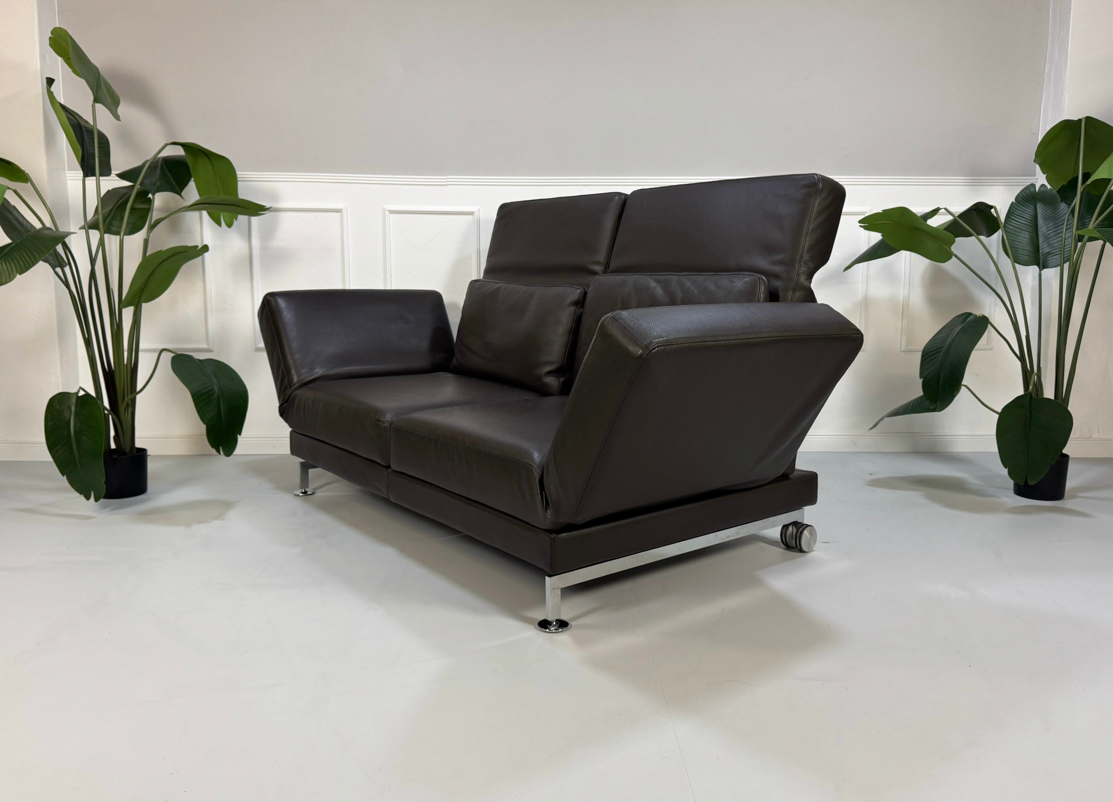 Gebrauchtes braunes Brühl Moule Designer Leder Sofa mit Schlaffunktion vor einer Wand, stilvoll und modern eingerichtet.