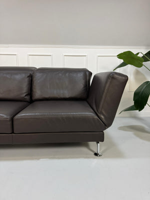 Gebrauchtes braunes Brühl Moule Designer Leder Sofa mit Schlaffunktion vor einer Wand, stilvoll und modern eingerichtet.