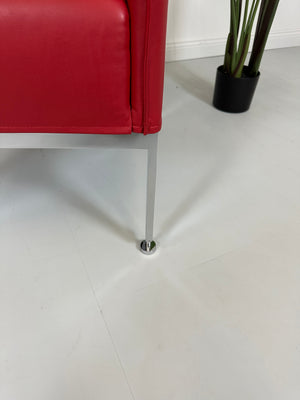 Gebrauchter roter Brühl Randolph Designer Leder Sessel vor einer Wand, stilvoll und modern eingerichtet.