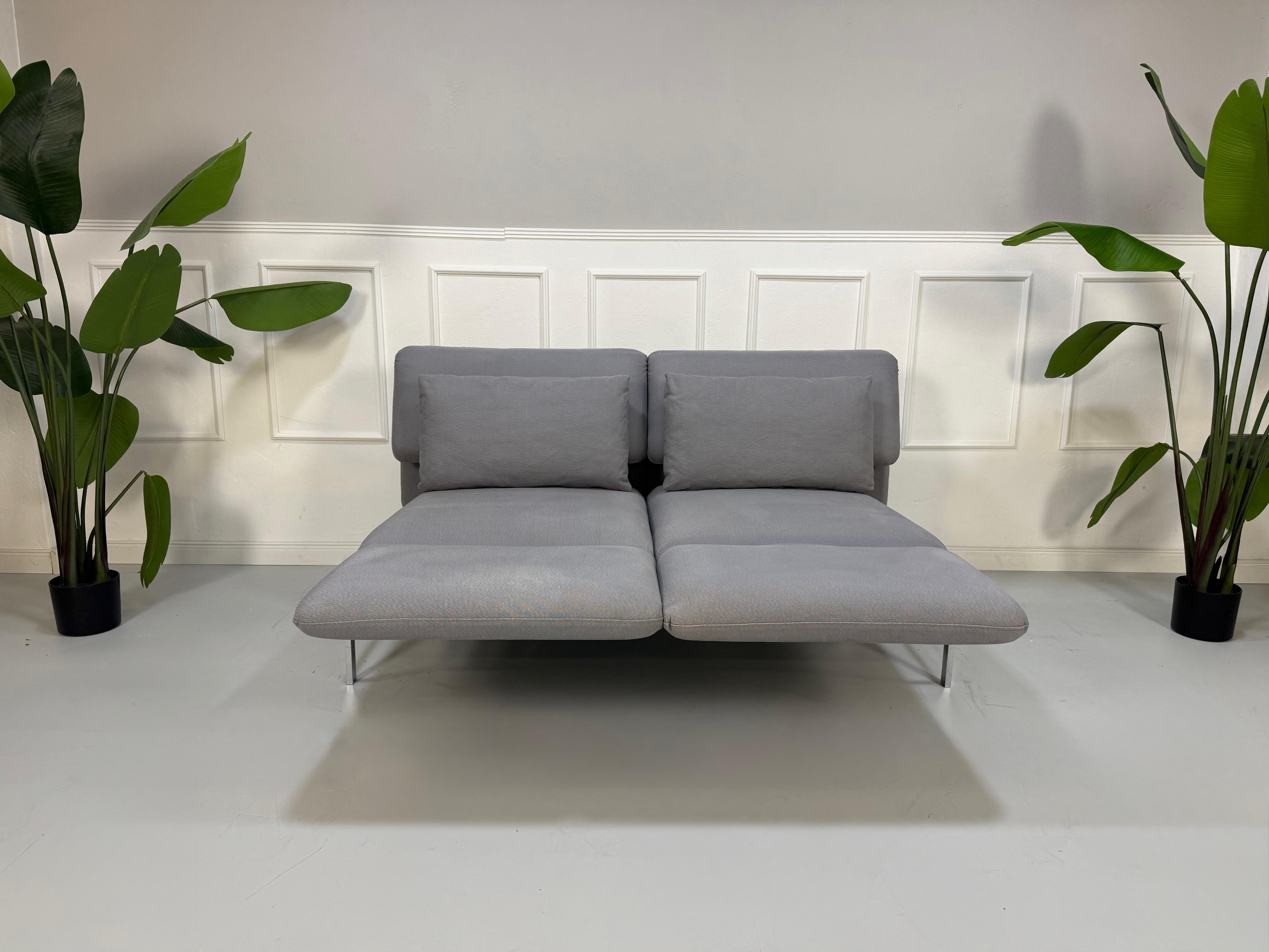 Erneuertes Brühl Roro Designer Stoff Sofa in der Farbe Grau vor einer Wand, stilvoll und modern eingerichtet.