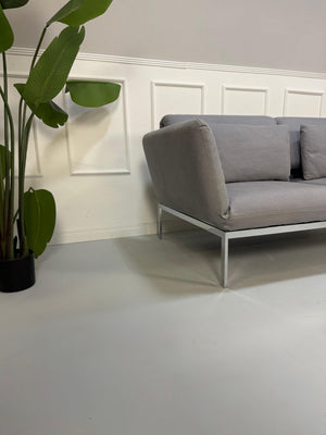 Erneuertes Brühl Roro Designer Stoff Sofa in der Farbe Grau vor einer Wand, stilvoll und modern eingerichtet.