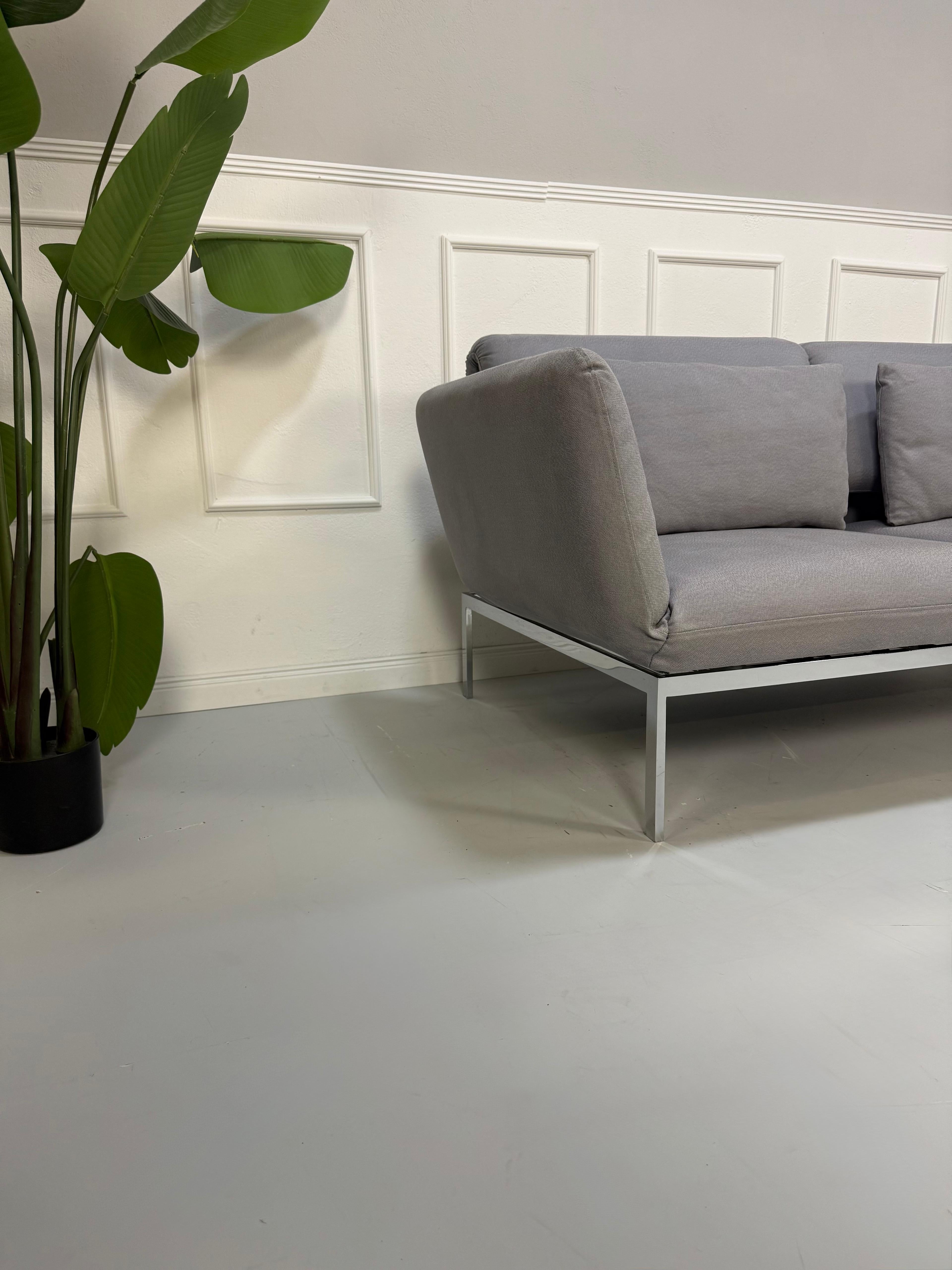 Erneuertes Brühl Roro Designer Stoff Sofa in der Farbe Grau vor einer Wand, stilvoll und modern eingerichtet.