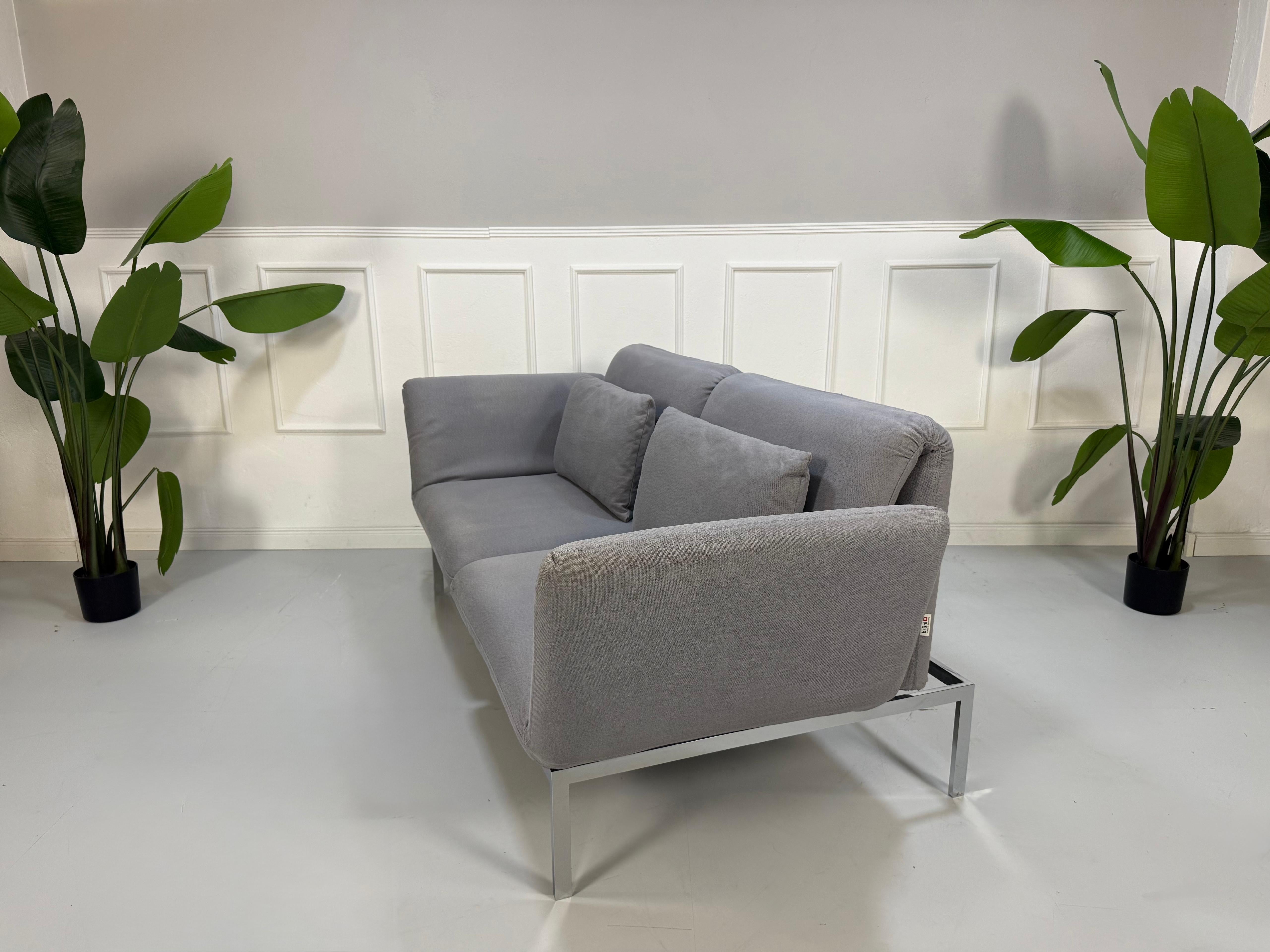 Erneuertes Brühl Roro Designer Stoff Sofa in der Farbe Grau vor einer Wand, stilvoll und modern eingerichtet.