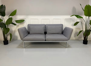 Erneuertes Brühl Roro Designer Stoff Sofa in der Farbe Grau vor einer Wand, stilvoll und modern eingerichtet.