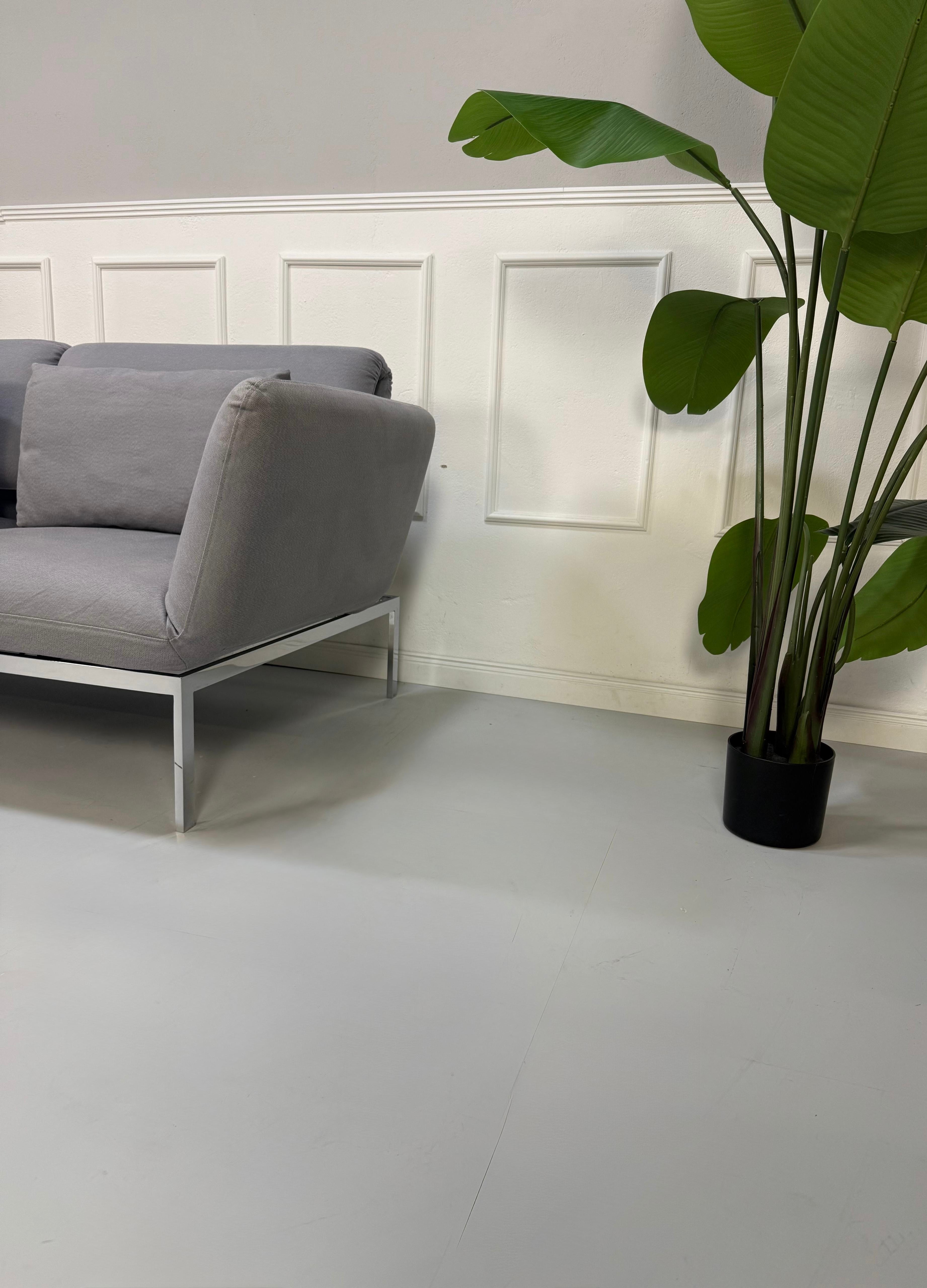 Erneuertes Brühl Roro Designer Stoff Sofa in der Farbe Grau vor einer Wand, stilvoll und modern eingerichtet.