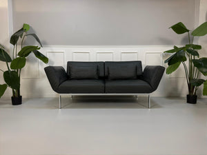 Erneuertes graues Brühl Roro Soft Designer Leder Sofa vor einer Wand, stilvoll und modern eingerichtet.