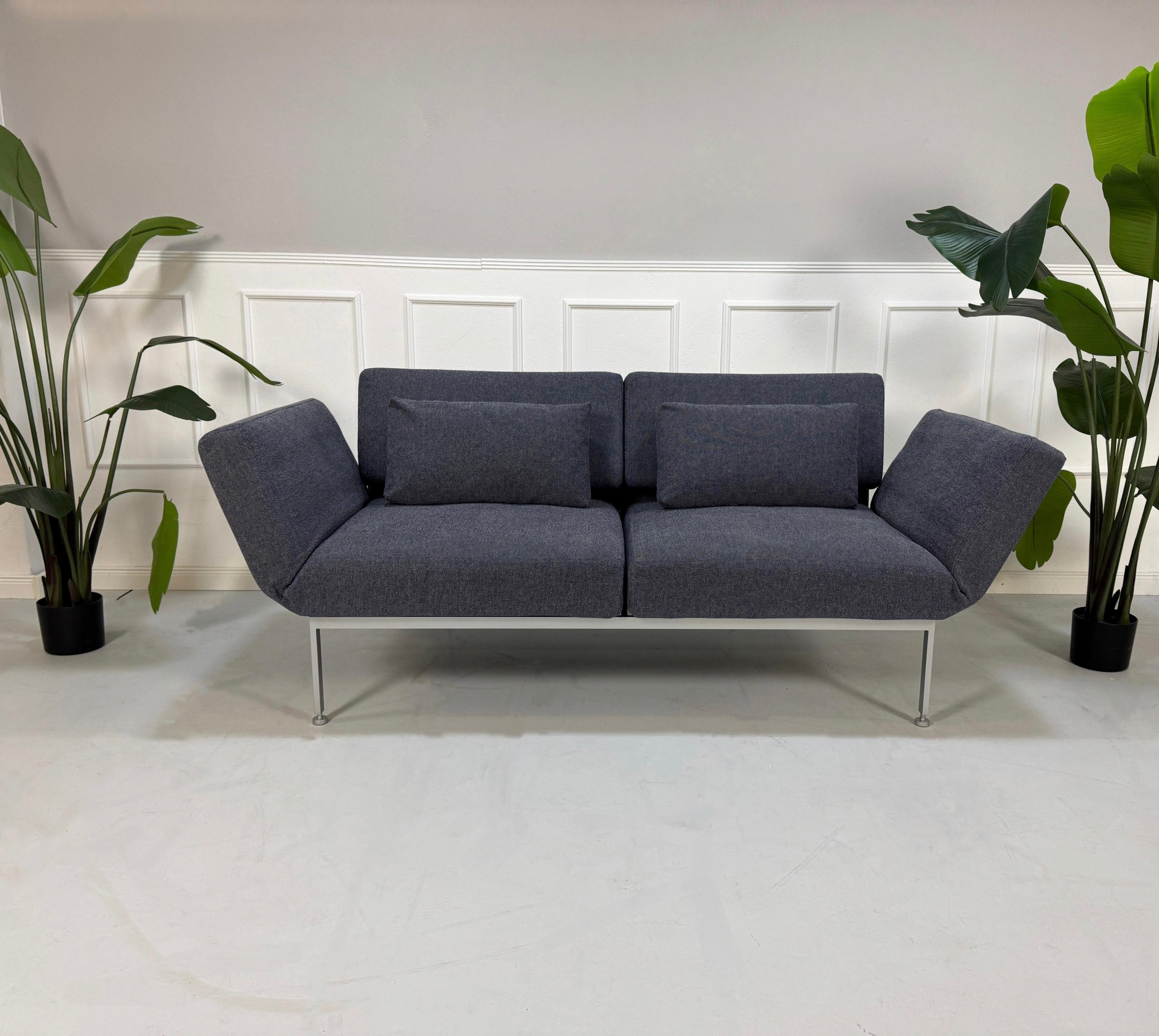 Gebrauchtes grau blaues Brühl Roro Soft Designer Stoff Sofa vor einer Wand, stilvoll und modern eingerichtet.