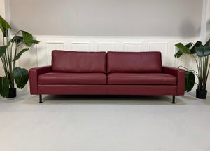 Gebrauchtes rotes COR Conseta Designer Leder Sofa vor einer Wand, stilvoll und modern eingerichtet.
