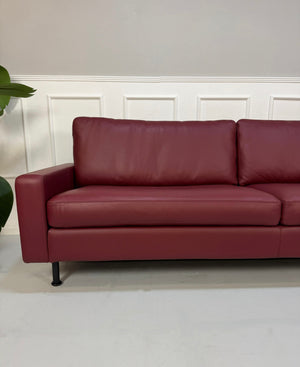 Gebrauchtes rotes COR Conseta Designer Leder Sofa vor einer Wand, stilvoll und modern eingerichtet.