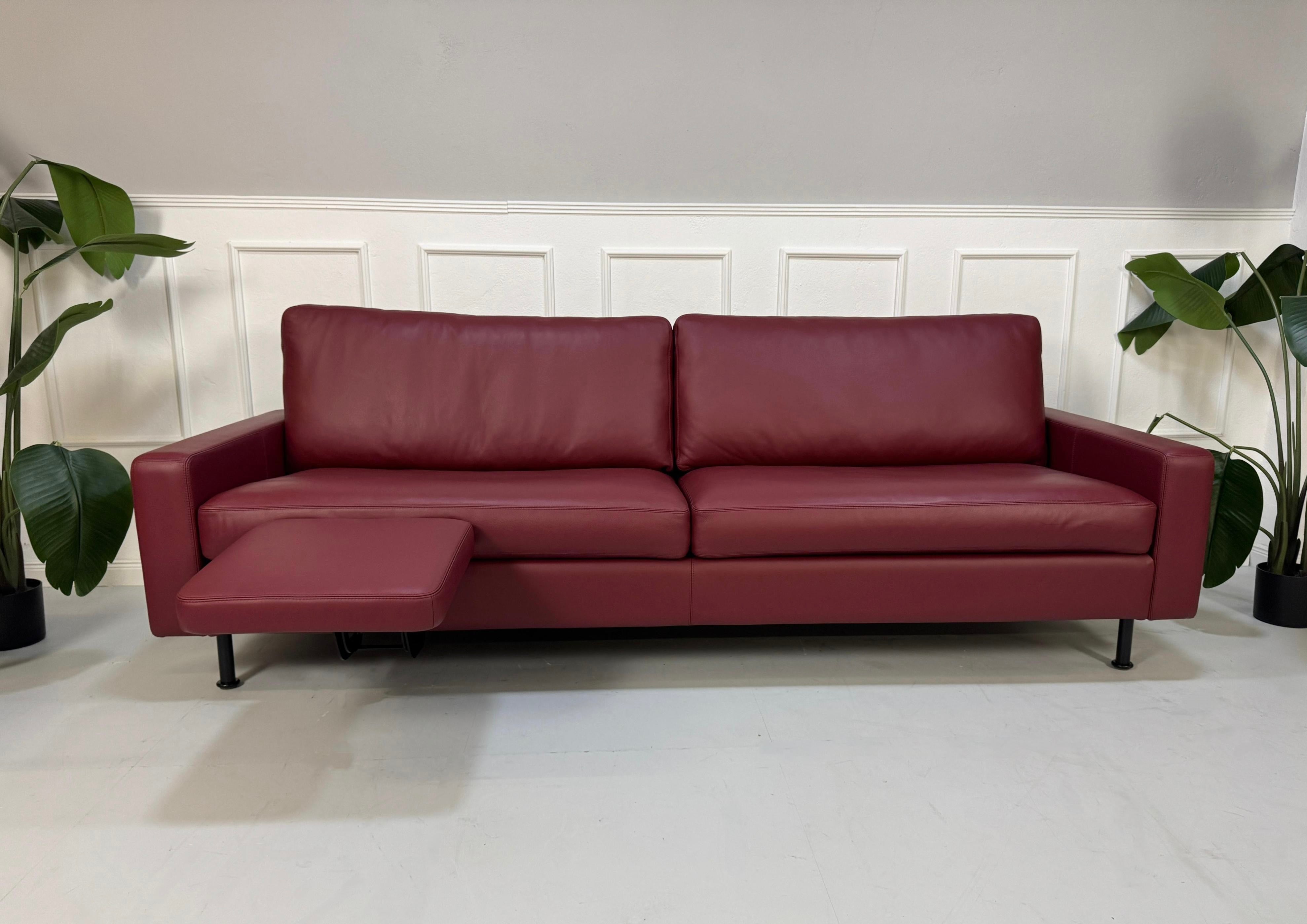 Gebrauchtes rotes COR Conseta Designer Leder Sofa vor einer Wand, stilvoll und modern eingerichtet.