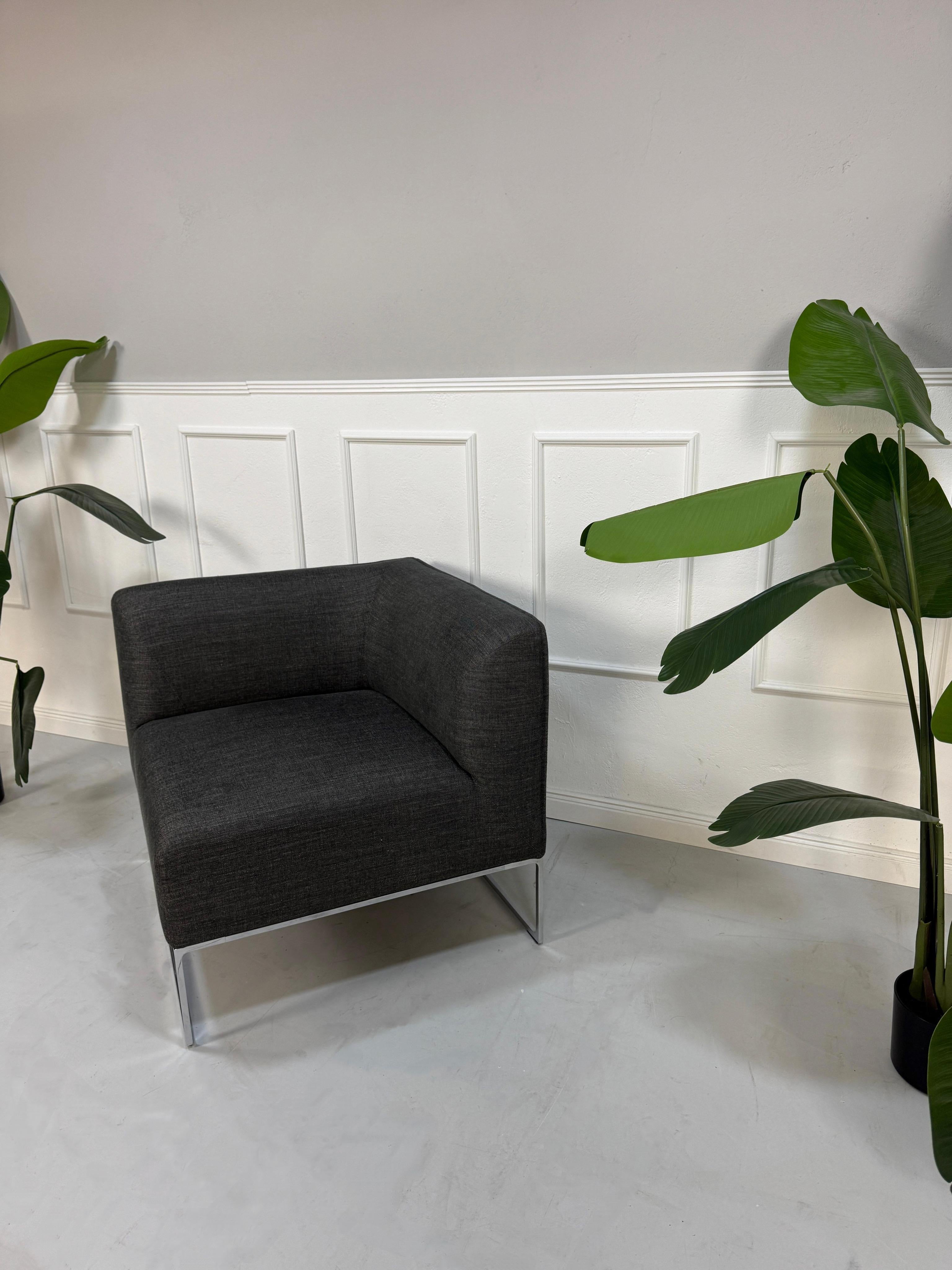 Gebrauchtes graues COR Mell Designer Stoff Sofa vor einer Wand, stilvoll und modern eingerichtet.
