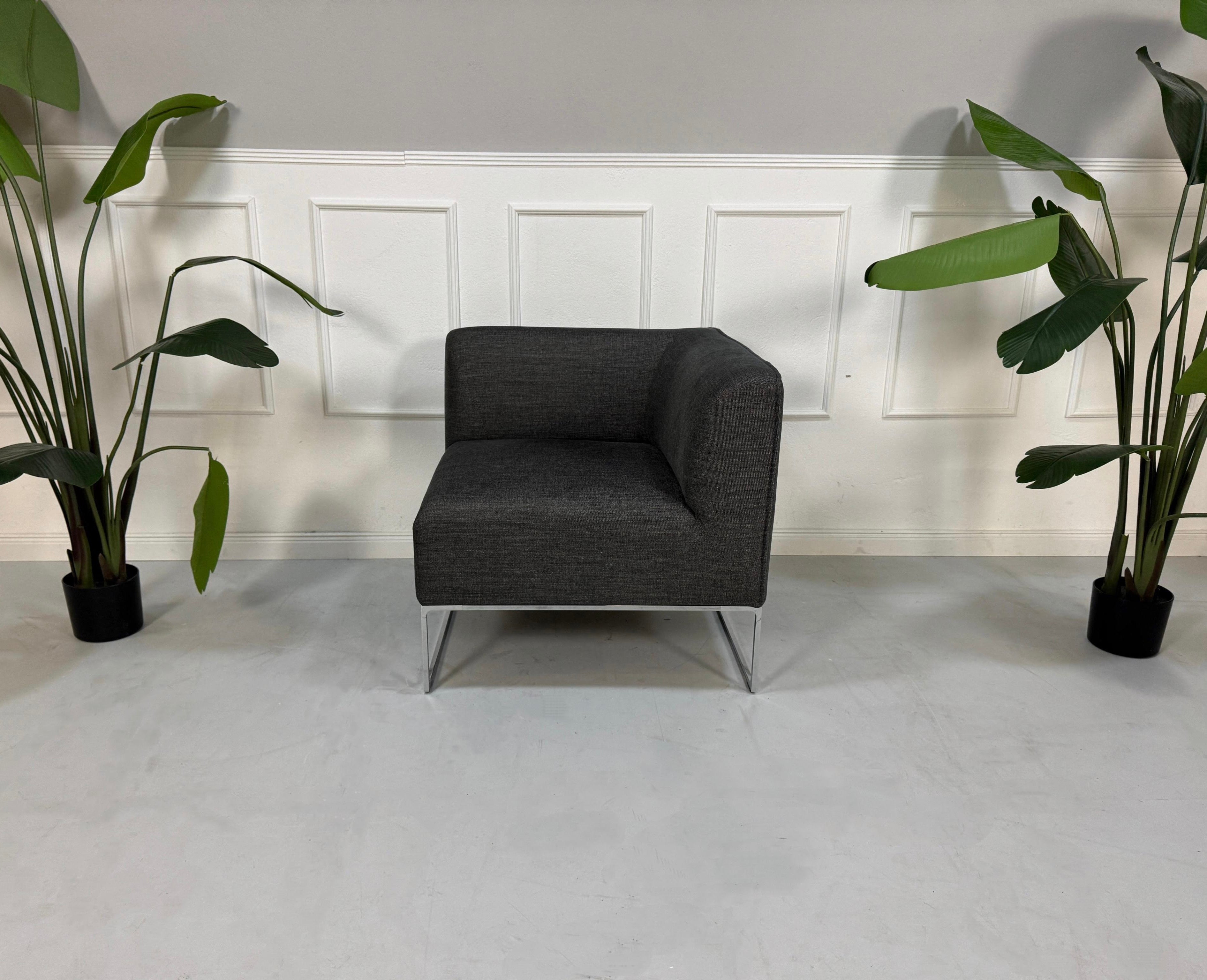 Gebrauchtes graues COR Mell Designer Stoff Sofa vor einer Wand, stilvoll und modern eingerichtet.