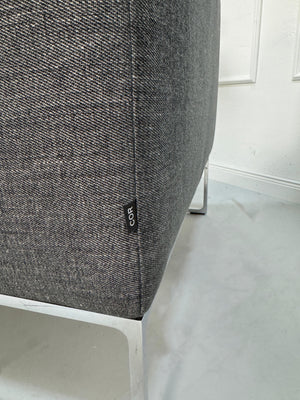 Gebrauchtes graues COR Mell Designer Stoff Sofa vor einer Wand, stilvoll und modern eingerichtet.