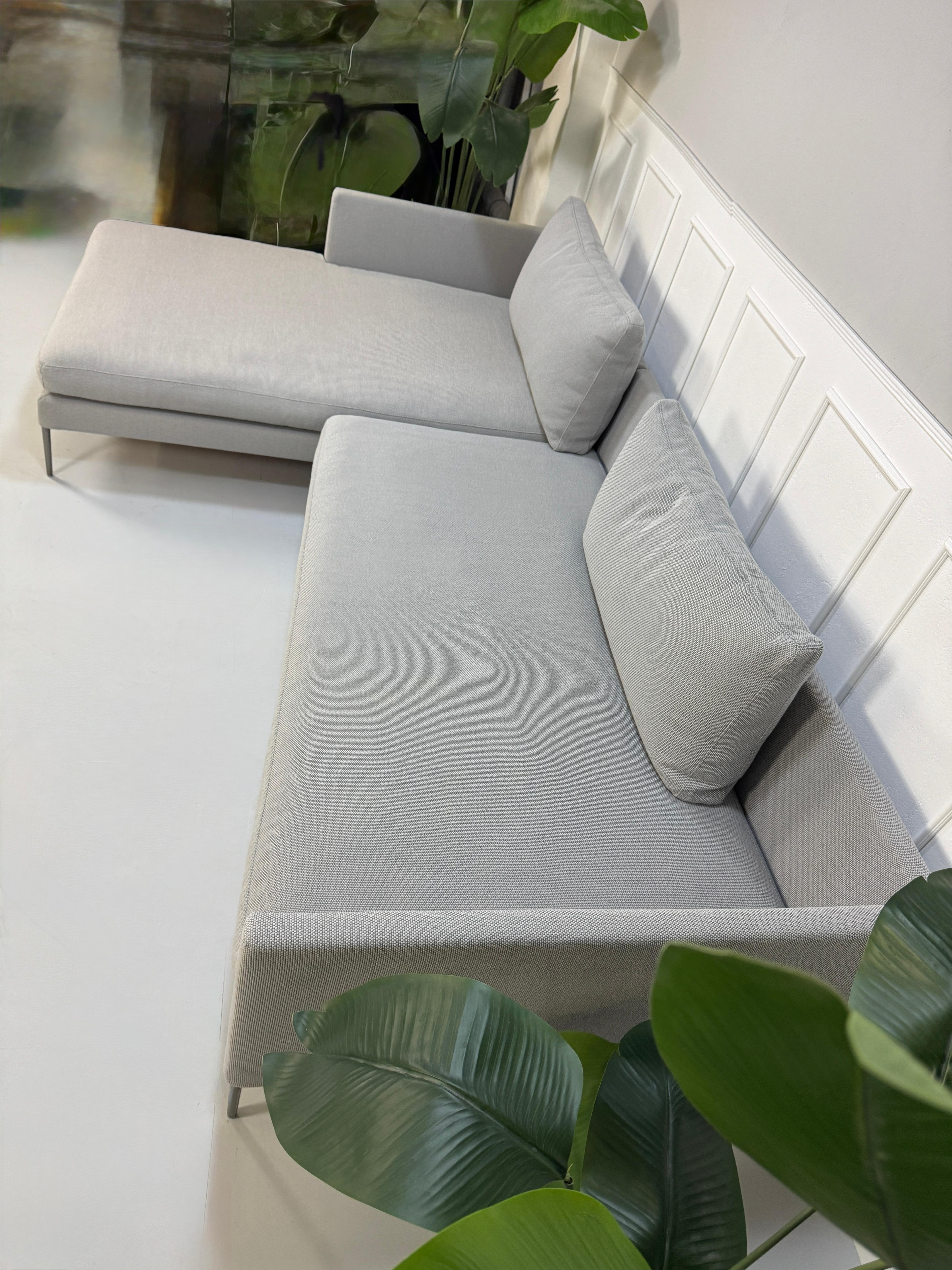 Gebrauchtes graues COR Pilotis Designer Stoff Sofa vor einer Wand, stilvoll und modern eingerichtet.
