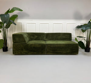 Gebrauchtes grünes COR Trio Designer Stoff Sofa vor einer Wand, stilvoll und modern eingerichtet.