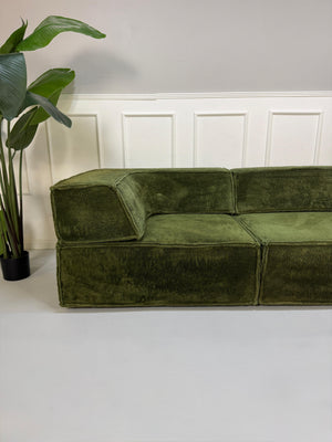 Gebrauchtes grünes COR Trio Designer Stoff Sofa vor einer Wand, stilvoll und modern eingerichtet.