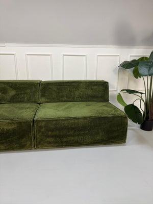 Gebrauchtes grünes COR Trio Designer Stoff Sofa vor einer Wand, stilvoll und modern eingerichtet.