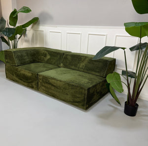 Gebrauchtes grünes COR Trio Designer Stoff Sofa vor einer Wand, stilvoll und modern eingerichtet.