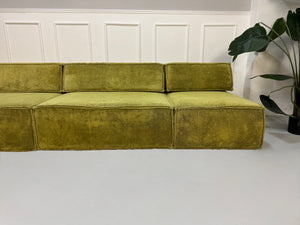 Gebrauchtes grünes Stoffsofa COR Modell Trio vor einer modernen Wand.