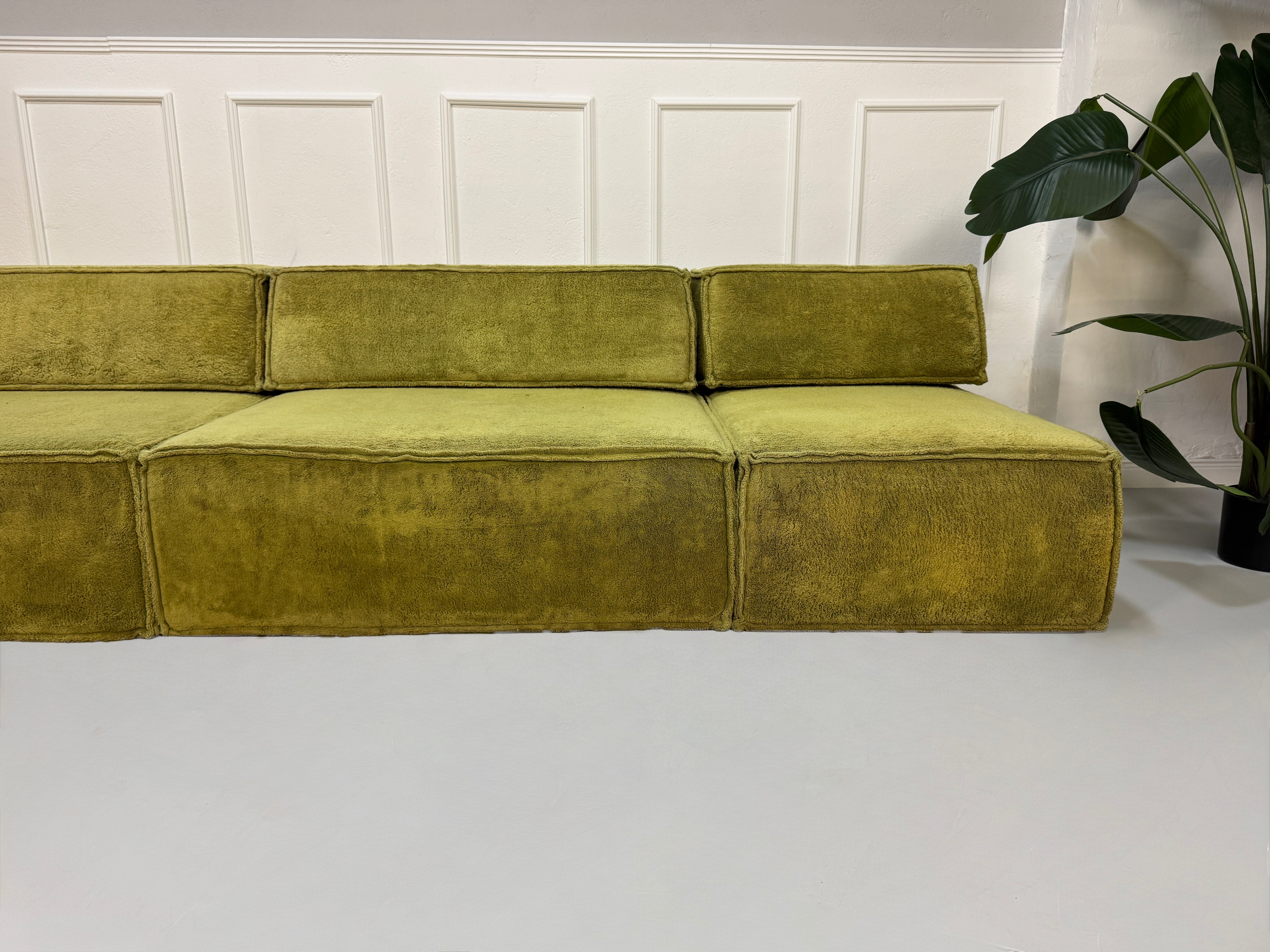 Gebrauchtes grünes Stoffsofa COR Modell Trio vor einer modernen Wand.