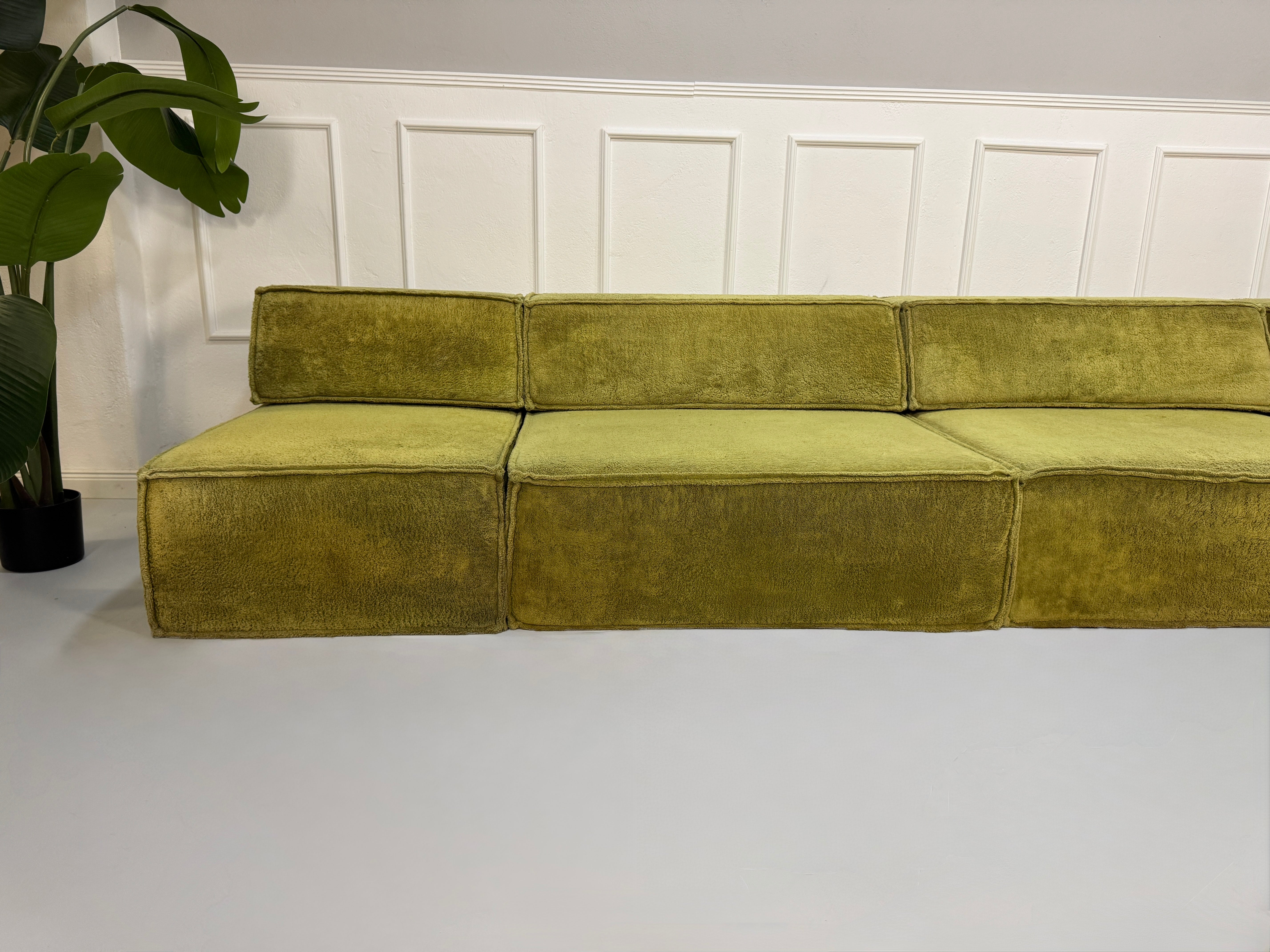 Gebrauchtes grünes Stoffsofa COR Modell Trio vor einer modernen Wand.