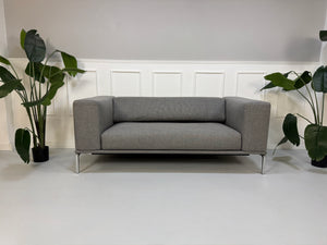 Gebrauchtes graues Cassina Moov Zweisitzer Designer Stoff Sofa vor einer Wand, stilvoll und modern eingerichtet.