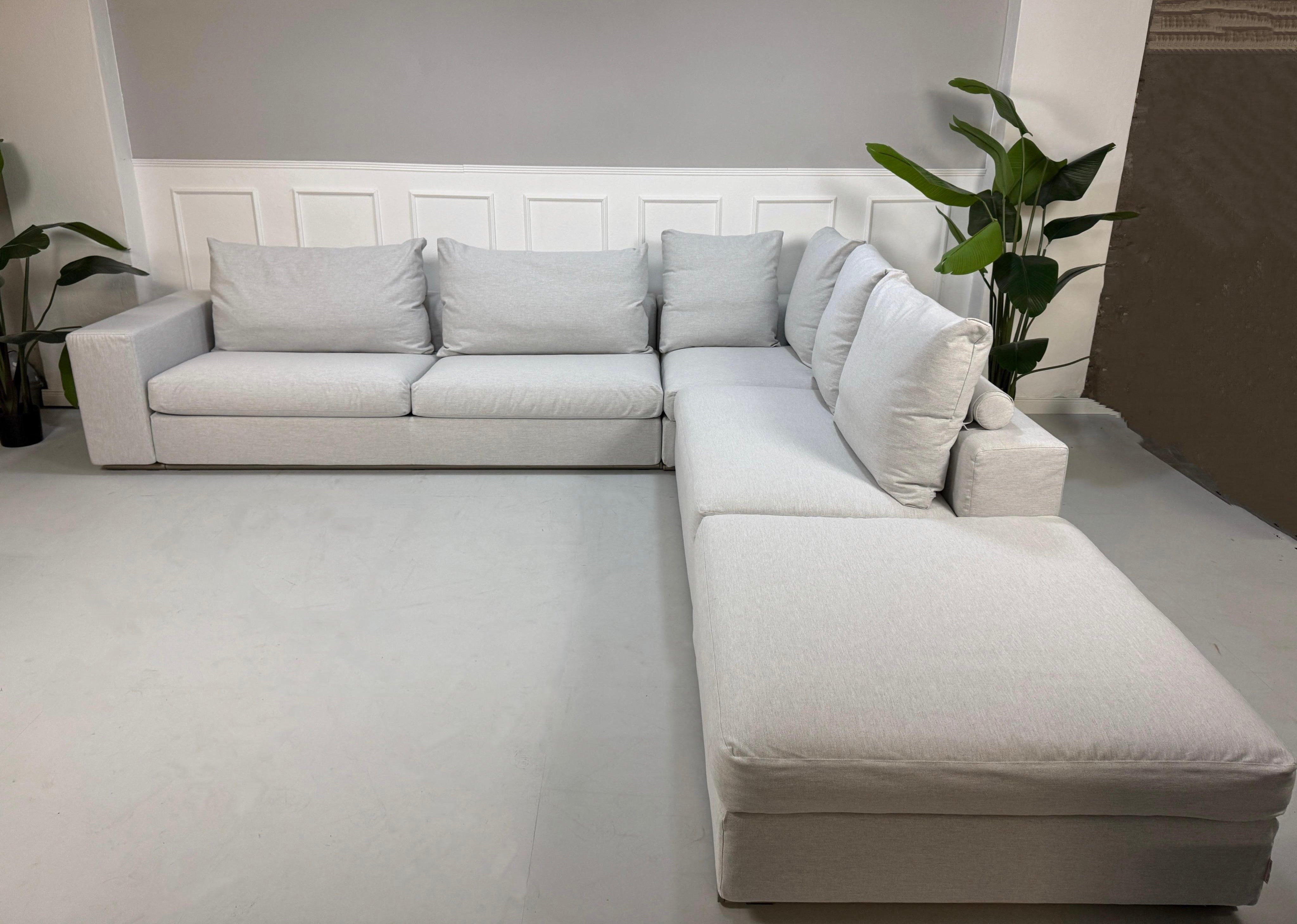 Gebrauchtes graues Flexform Groundpiece Designer Stoff Sofa vor einer Wand, stilvoll und modern eingerichtet.