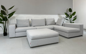 Gebrauchtes graues Flexform Groundpiece Designer Stoff Sofa mit Hocker vor einer Wand, stilvoll und modern eingerichtet.