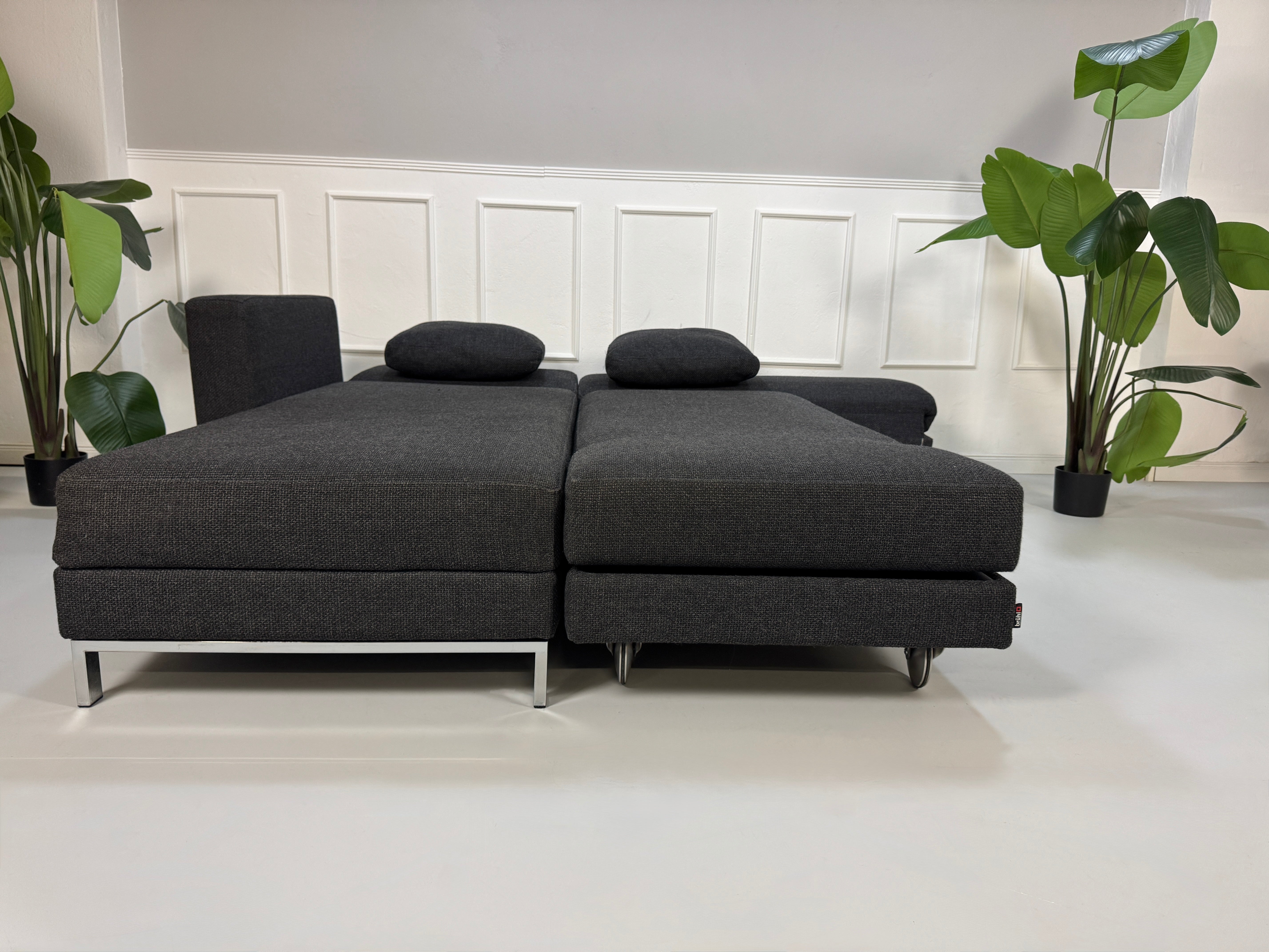 Gebrauchtes graues Stoffsofa Brühl Modell FourTwo vor einer modernen Wand.