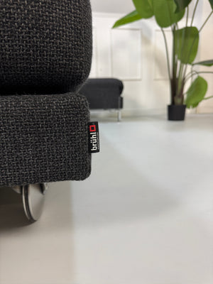 Gebrauchtes graues Stoffsofa Brühl Modell FourTwo vor einer modernen Wand.
