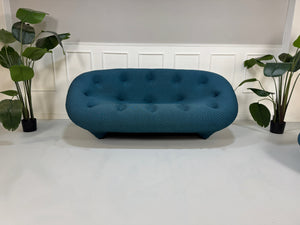 Gebrauchtes blaues Ligne Roset Ploum Designer Stoff Sofa mit Hocker vor einer Wand, stilvoll und modern eingerichtet.
