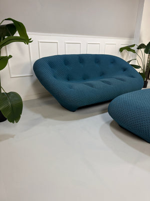 Gebrauchtes blaues Ligne Roset Ploum Designer Stoff Sofa mit Hocker vor einer Wand, stilvoll und modern eingerichtet.