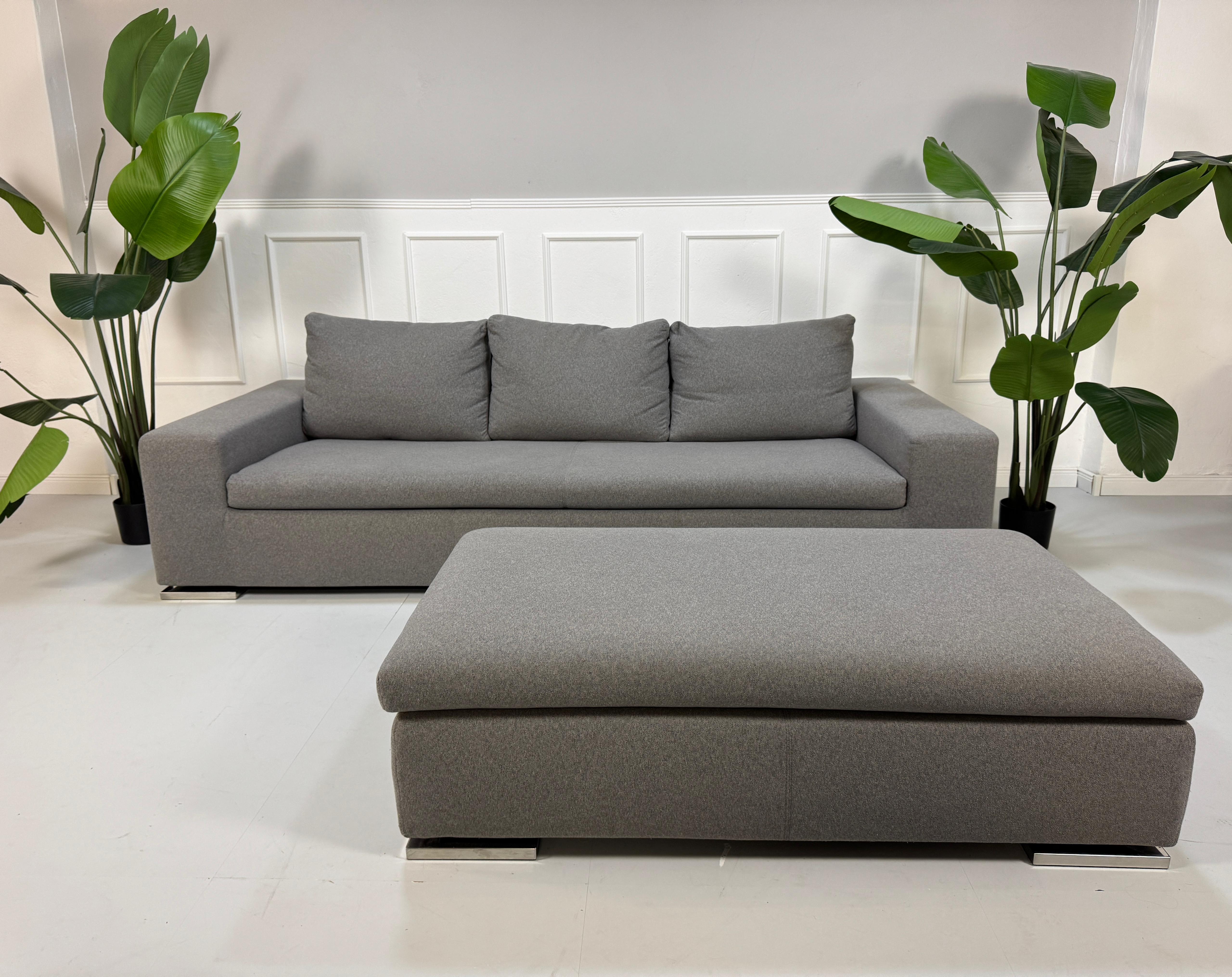 Gebrauchtes Minotti Moore Stoff Sofa mit einem Hocker in der Farbe Grau vor einer Wand, stilvoll und modern eingerichtet.