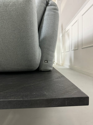 Gebrauchtes grau blaues Rolf Benz Aura Designer Stoff Sofa vor einer Wand, stilvoll und modern eingerichtet.