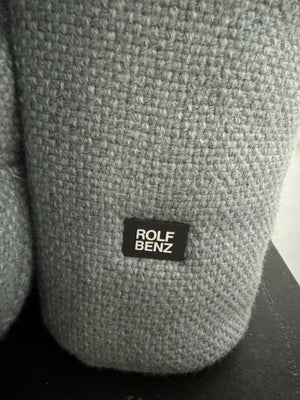 Gebrauchtes grau blaues Rolf Benz Aura Designer Stoff Sofa vor einer Wand, stilvoll und modern eingerichtet.