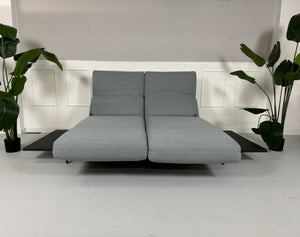Gebrauchtes grau blaues Rolf Benz Aura Designer Stoff Sofa vor einer Wand, stilvoll und modern eingerichtet.