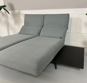 Gebrauchtes grau blaues Rolf Benz Aura Designer Stoff Sofa vor einer Wand, stilvoll und modern eingerichtet.