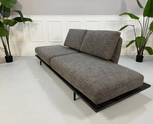 Gebrauchtes graues Rolf Benz Aura Designer Stoff Sofa vor einer Wand, stilvoll und modern eingerichtet.