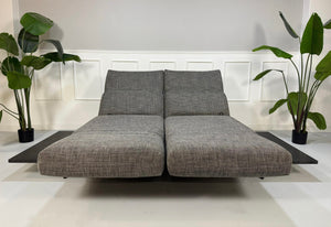 Gebrauchtes graues Rolf Benz Aura Designer Stoff Sofa vor einer Wand, stilvoll und modern eingerichtet.
