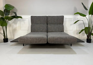 Gebrauchtes graues Rolf Benz Aura Designer Stoff Sofa vor einer Wand, stilvoll und modern eingerichtet.