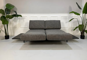 Gebrauchtes graues Rolf Benz Aura Designer Stoff Sofa vor einer Wand, stilvoll und modern eingerichtet.