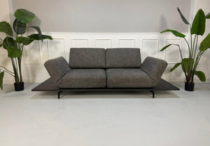 Gebrauchtes graues Rolf Benz Aura Designer Stoff Sofa vor einer Wand, stilvoll und modern eingerichtet.