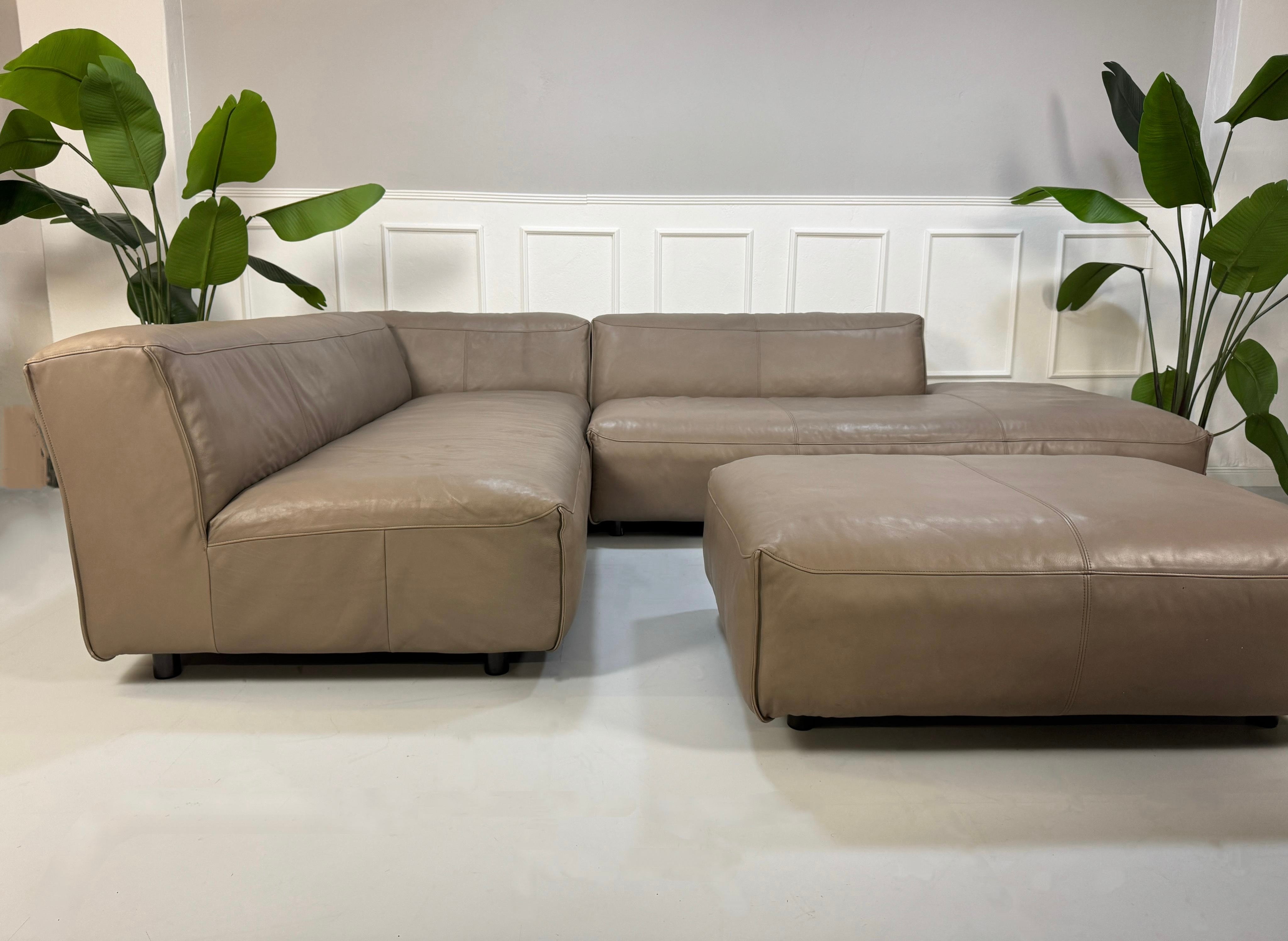Gebrauchtes Rolf Benz Mio mit Hocker Designer Leder Sofa vor einer Wand, stilvoll und modern eingerichtet.