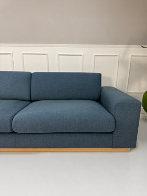 Gebrauchtes blaues Bolia Sepia Designer Stoff Sofa vor einer Wand, stilvoll und modern eingerichtet.