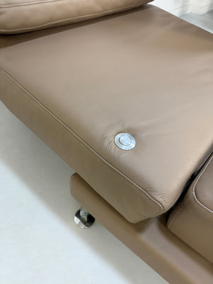 Gebrauchtes braunes Brühl Moule Medium Designer Leder Sofa vor einer Wand, stilvoll und modern eingerichtet.