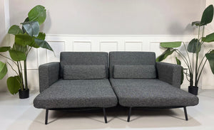 Gebrauchtes graues Studio Copenhagen Copperfield Designer Stoff Sofa vor einer Wand, stilvoll und modern eingerichtet.