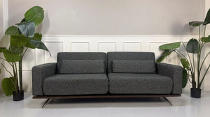 Gebrauchtes graues Studio Copenhagen Copperfield Designer Stoff Sofa vor einer Wand, stilvoll und modern eingerichtet.